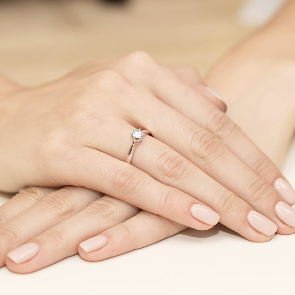 W0234.R3.DIW.04_4 Na dłoni z delikatnym manicure znajduje się pierścionek z okrągłym diamentem.