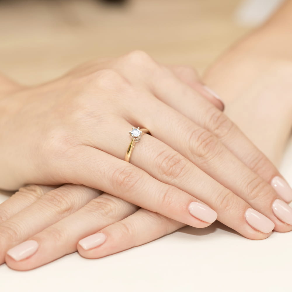 W0234.Z3.LDW.04_4 Złoty pierścionek z diamentem na palcu, dłonie z delikatnym manicure w jasnym kolorze.