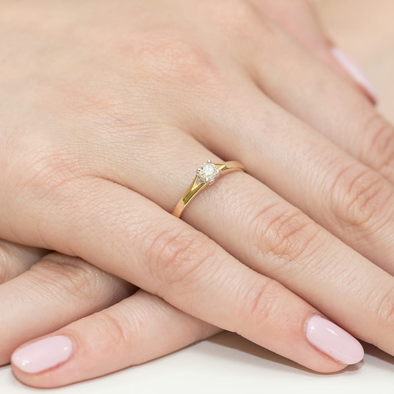 W0240.Z3.LDW.01_4 Złoty pierścionek z diamentem na palcu kobiety, z delikatnym manicure w jasnym kolorze.