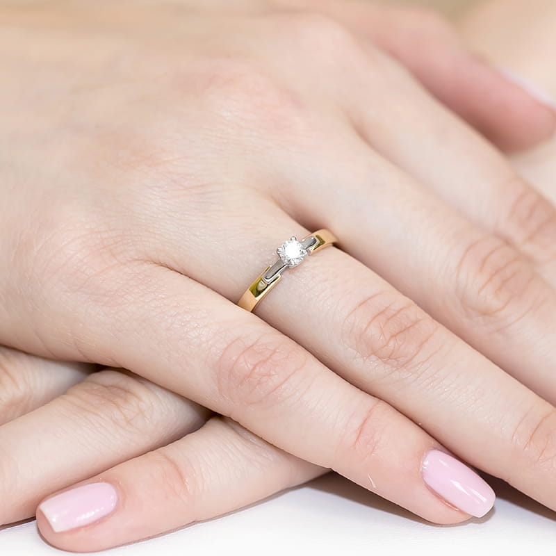 W0241.Z3.DIW.03_4 Złoty pierścionek z diamentem na palcu, dłonie z delikatnym manicure w jasnym kolorze.