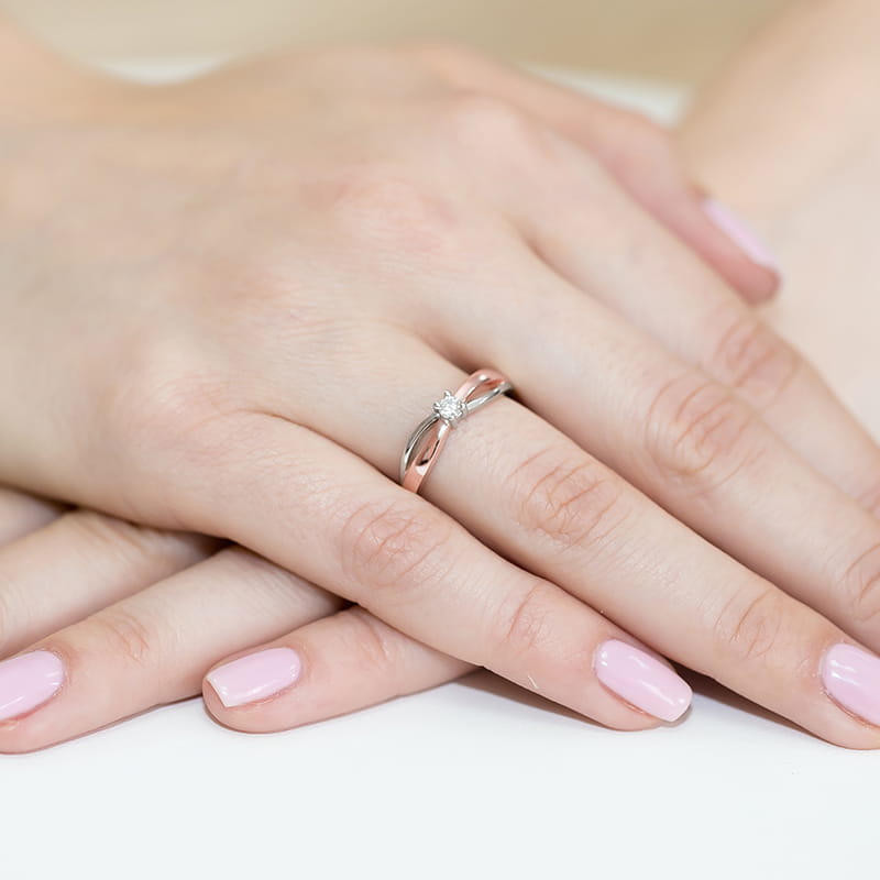 W0248.R3.LDW.01_4 Na dłoni z różowym manicure znajduje się srebrny pierścionek z diamentem.