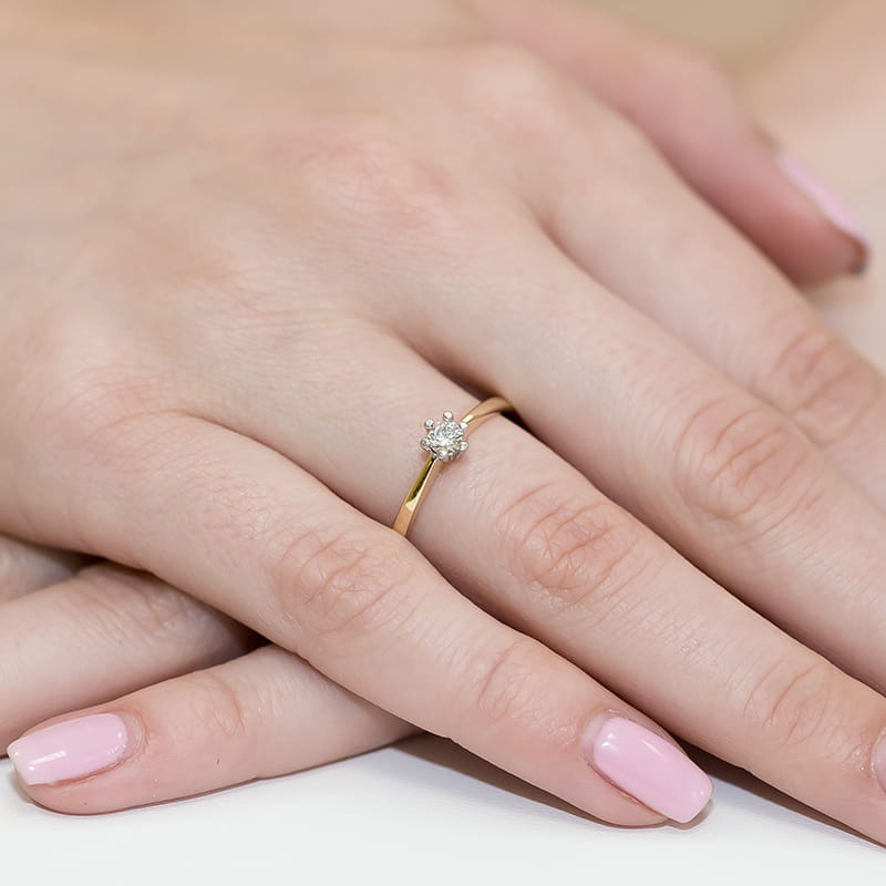 W0256.Z3.DIW.01_4 Złoty pierścionek z diamentem na palcu kobiecej ręki z różowym manicure.
