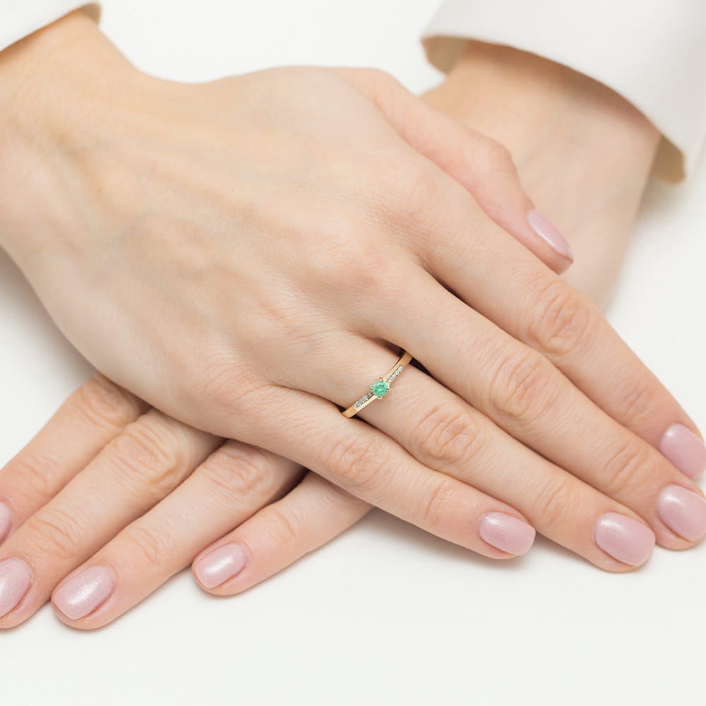 W0258.Z3.EMG.01_4 Złoty pierścionek z zielonym kamieniem na palcu, dłonie z delikatnym manicure w jasnym kolorze.