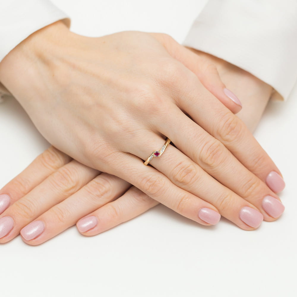W0262.Z3.RUR.01_4 Na dłoni z delikatnym manicure znajduje się złoty pierścionek z kolorowym kamieniem.