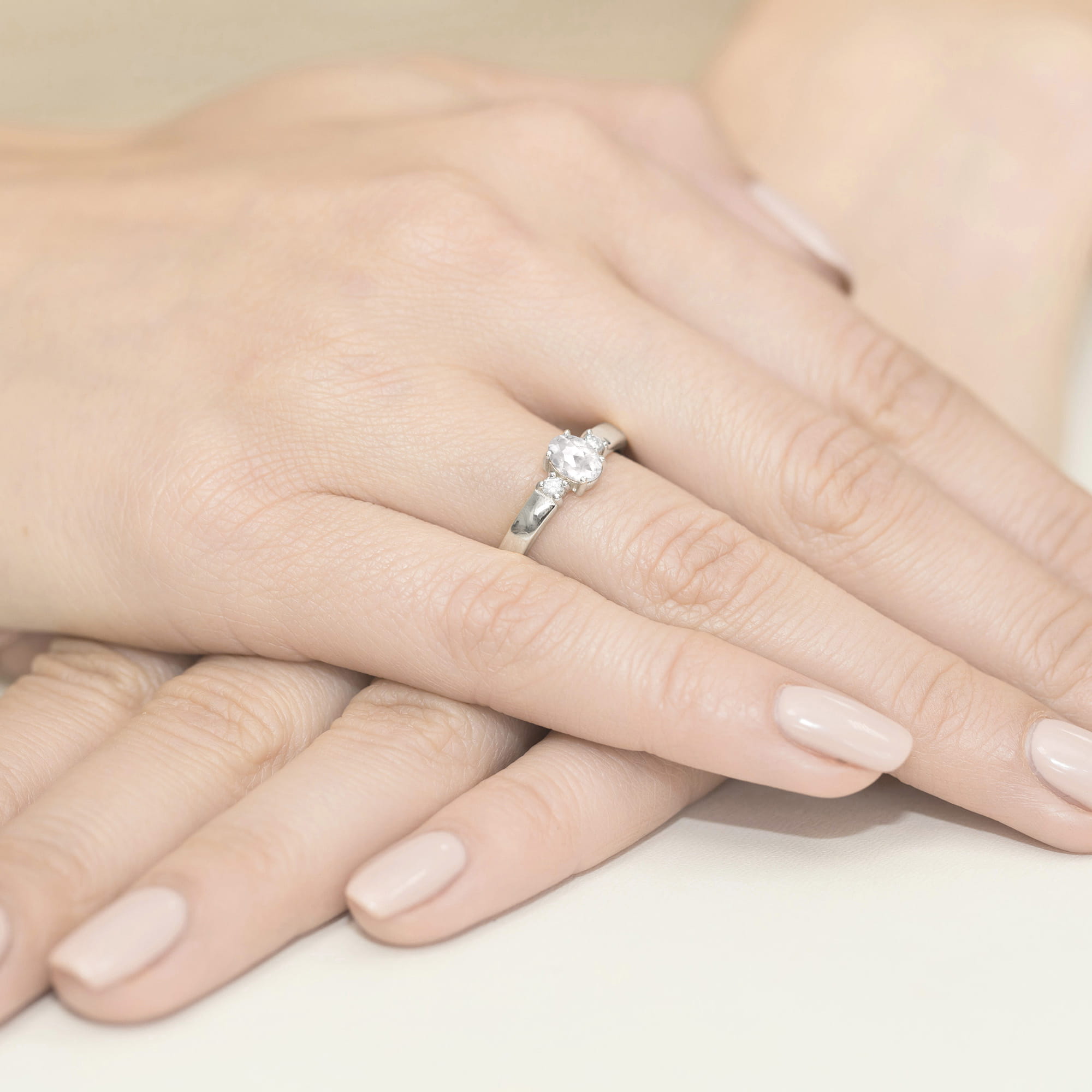 W0264.B3.LDW.01_4 Na dłoni widoczny pierścionek z diamentem, otoczony delikatnymi, zadbanymi palcami z jasnym manicure.