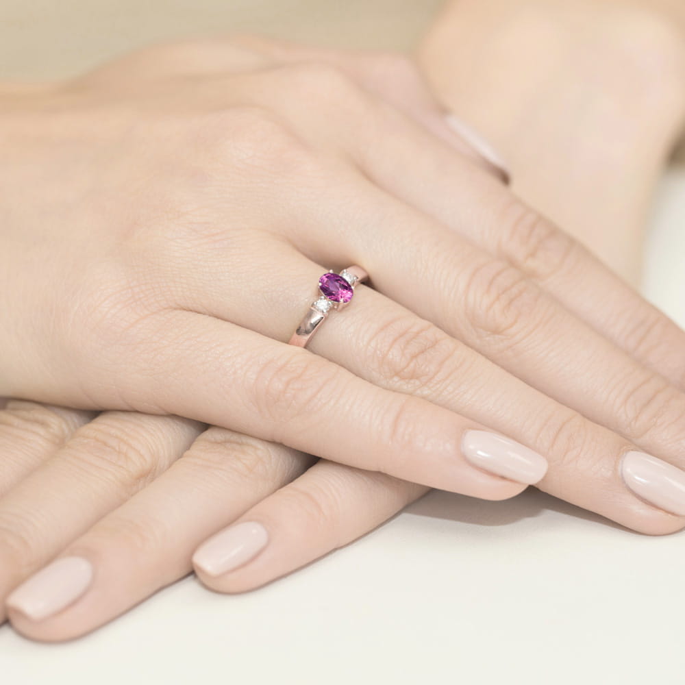 W0264.R3.SAP.01_4 Na dłoni znajduje się srebrny pierścionek z różowym kamieniem szlachetnym, otoczony delikatnymi palcami.