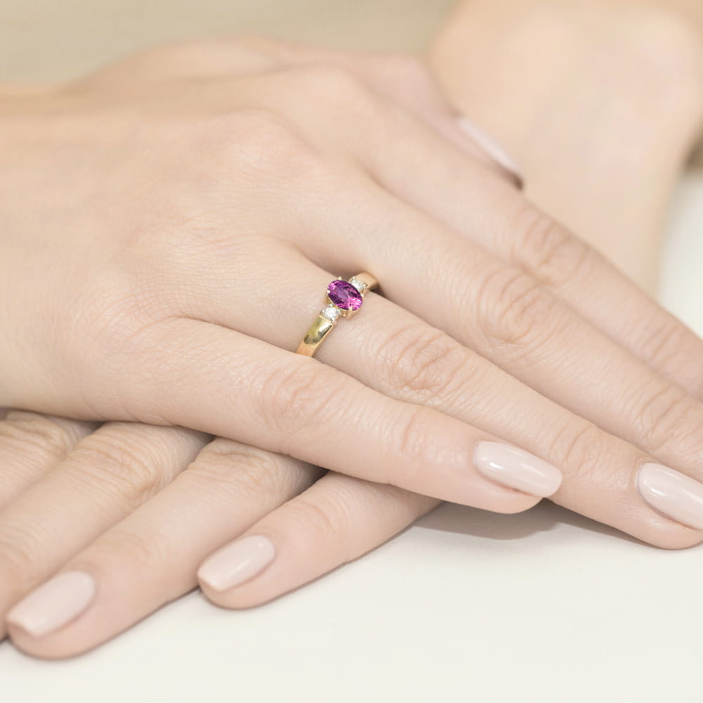 W0264.Z3.SAP.01_4 Złoty pierścionek z różowym kamieniem na palcu, dłonie z delikatnym manicure w jasnym kolorze.