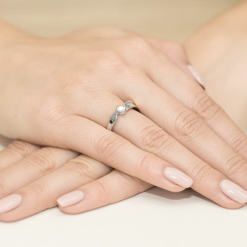 W0278.B3.LDW.01_4 Na dłoni z delikatnym manicure znajduje się srebrny pierścionek z diamentem.