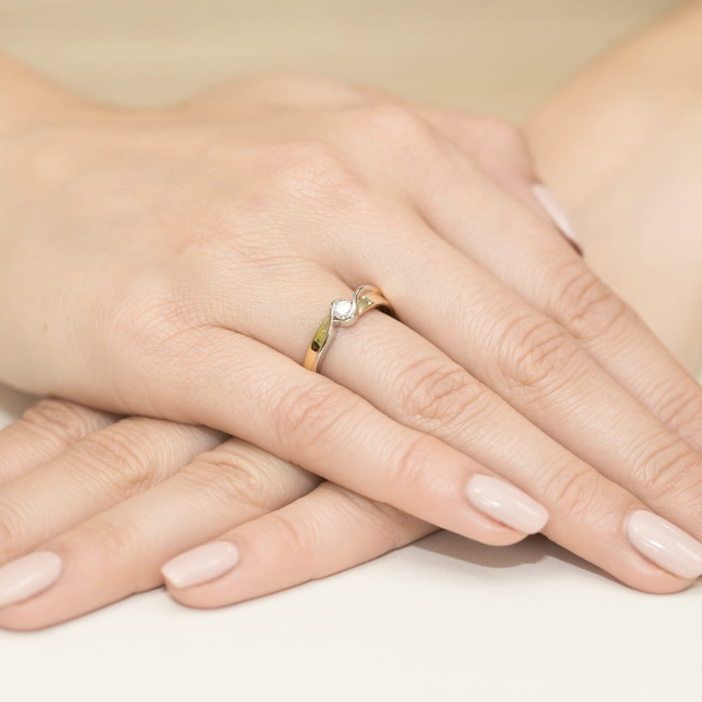 W0278.Z3.DIW.01_4 Złoty pierścionek z diamentem na palcu, dłonie z zadbanymi paznokciami w jasnym kolorze.