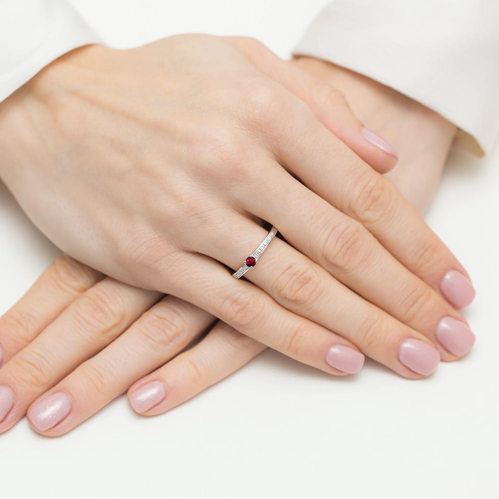 W0288.B3.RUR.01_4 Na dłoniach z delikatnym manicure znajduje się pierścionek z czerwonym kamieniem i diamentami.