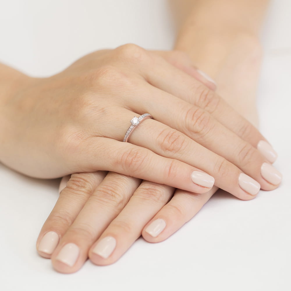 W0288.R3.DIW.02_4 Na dłoni z delikatnym manicure znajduje się pierścionek z małymi diamentami.