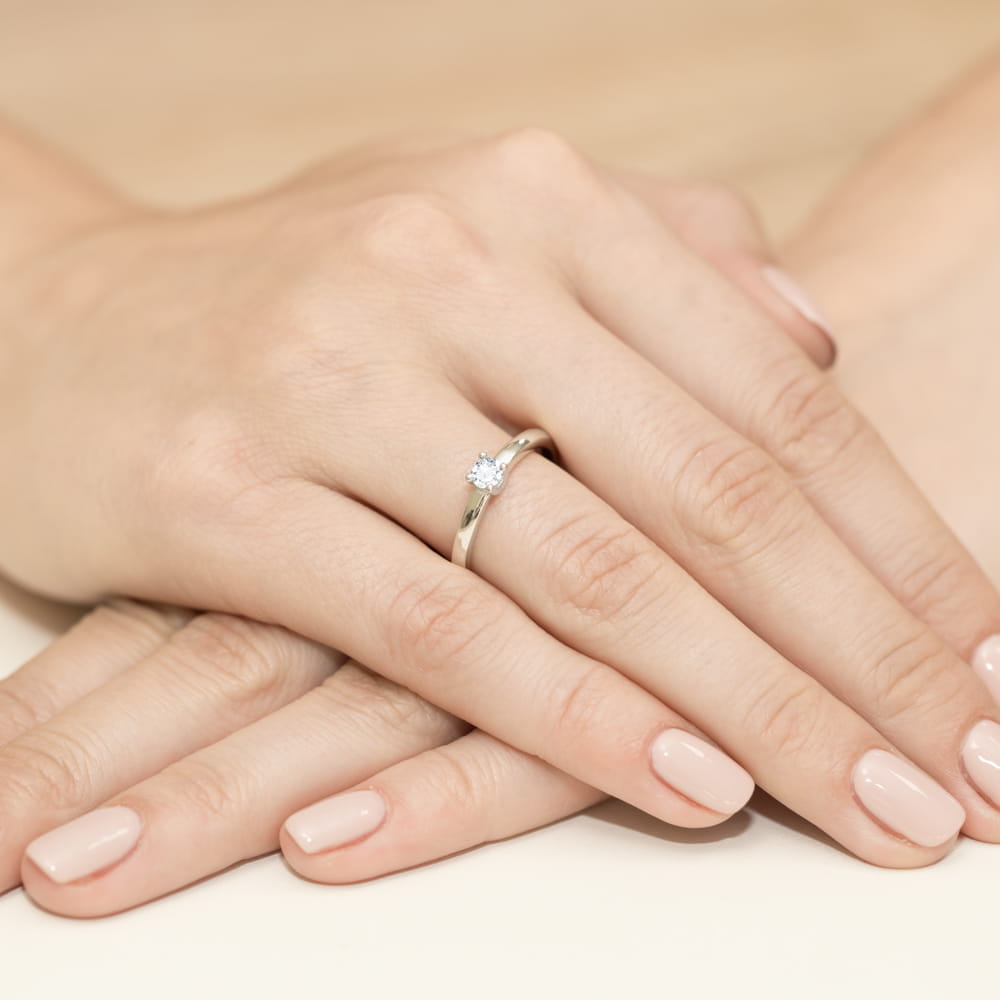 W0292.B3.DIW.01_4 Dwie ręce z delikatnym pierścionkiem na palcu, z zadbanymi paznokciami w jasnym kolorze.