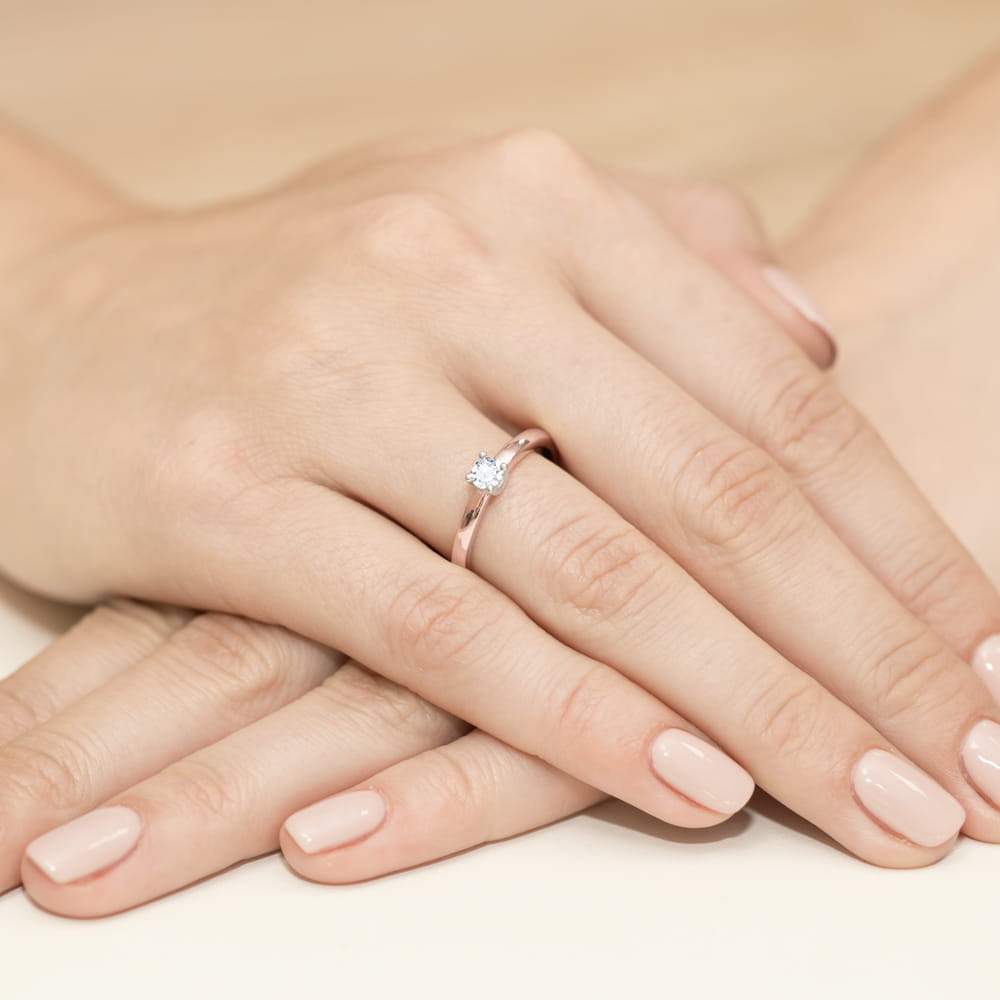 W0292.R3.LDW.02_4 Dwie ręce z delikatnym pierścionkiem z diamentem na palcu, z zadbanymi paznokciami w jasnym kolorze.