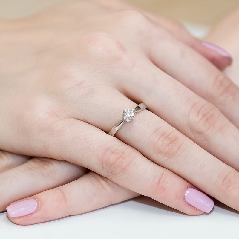 W0293.B3.DIW.01_4 Na dłoni z różowym manicure znajduje się srebrny pierścionek z dużym, okrągłym diamentem.