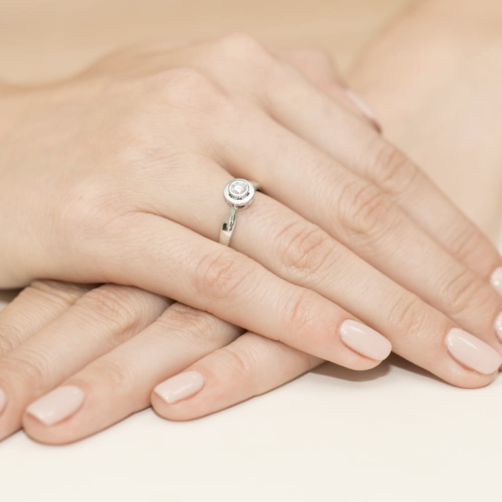 W0294.B3.DIW.05_4 Dwie dłonie z delikatnym pierścionkiem na palcu, z subtelnym zdobieniem i jasnym lakierem na paznokciach.