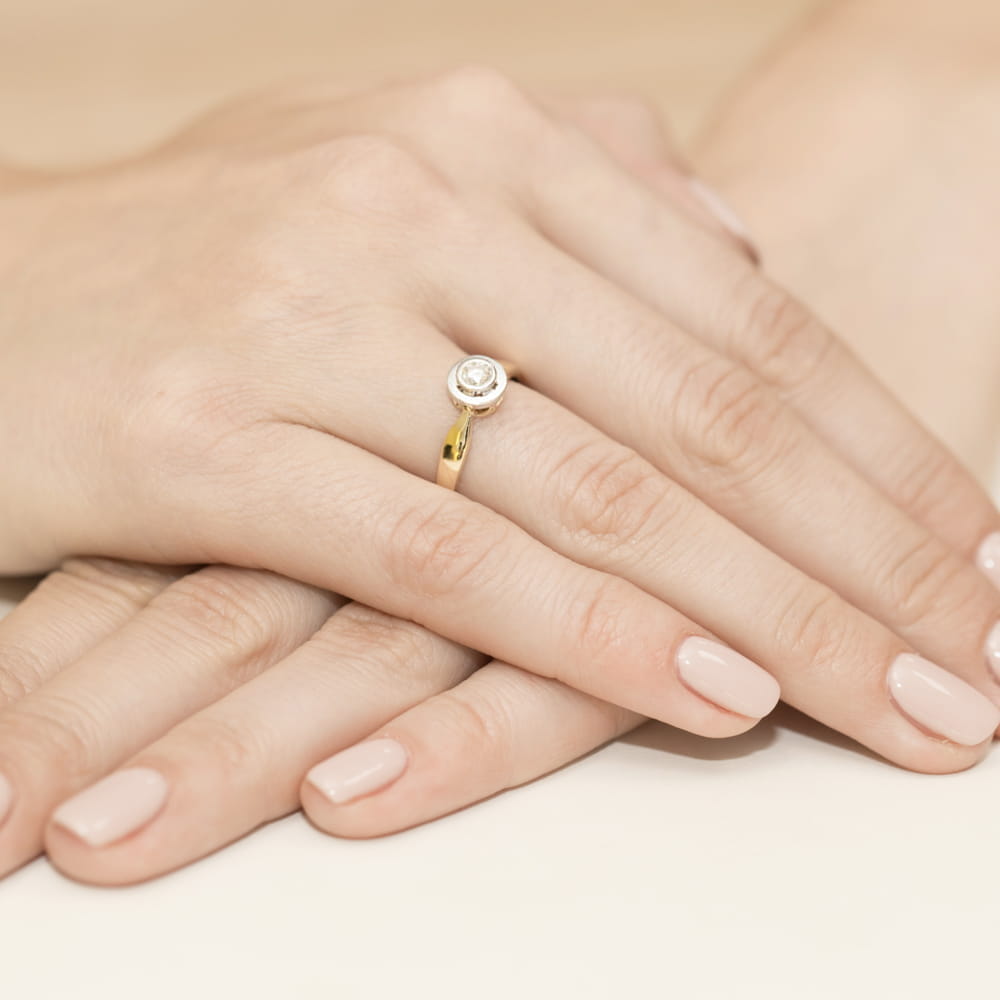 W0294.Z3.LDW.04_4 Złoty pierścionek z diamentem na palcu, dłonie z delikatnym manicure w jasnym kolorze.