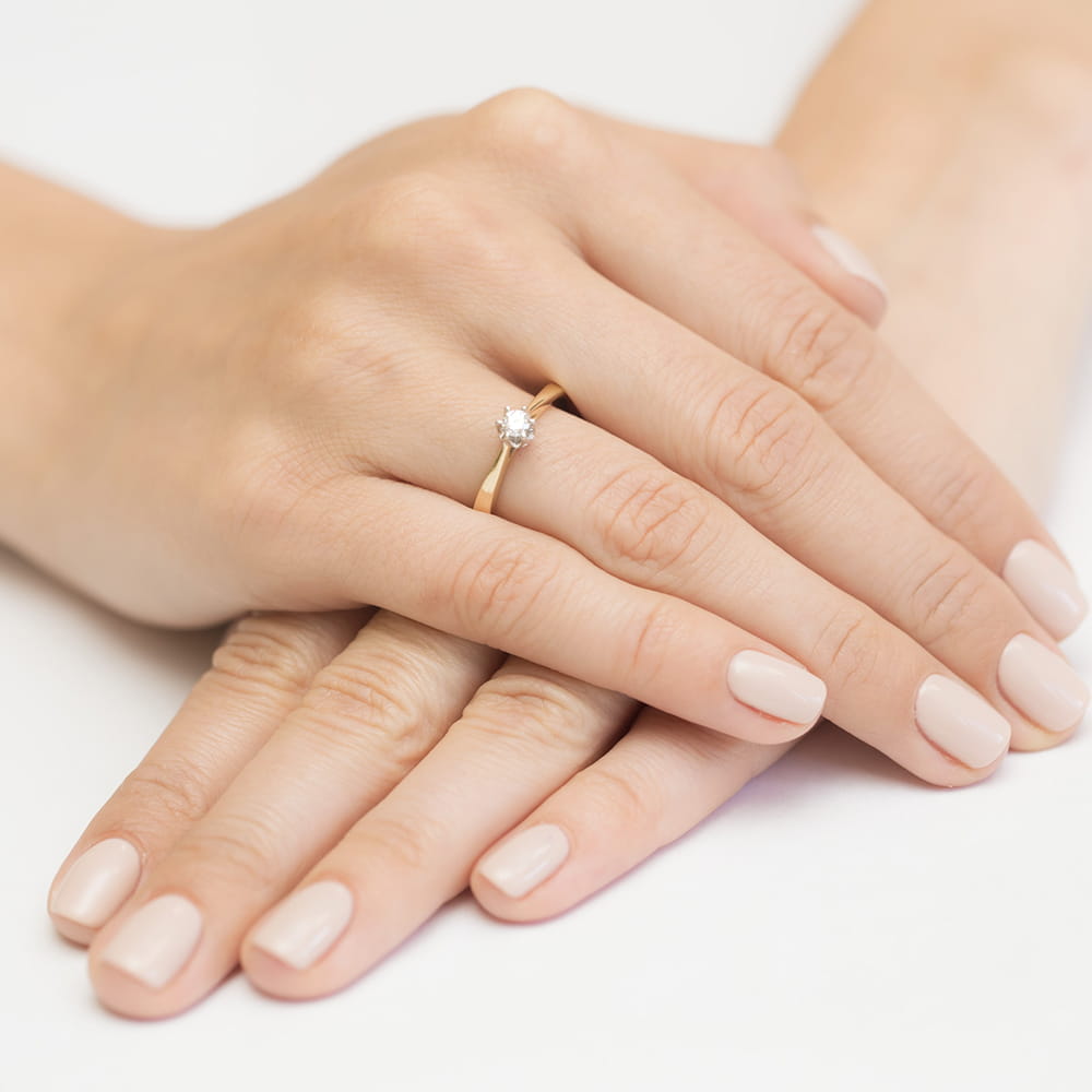 W0295.Z3.DIW.01_4 Na dłoni z delikatnym manicure znajduje się złoty pierścionek z dużym, błyszczącym kamieniem.