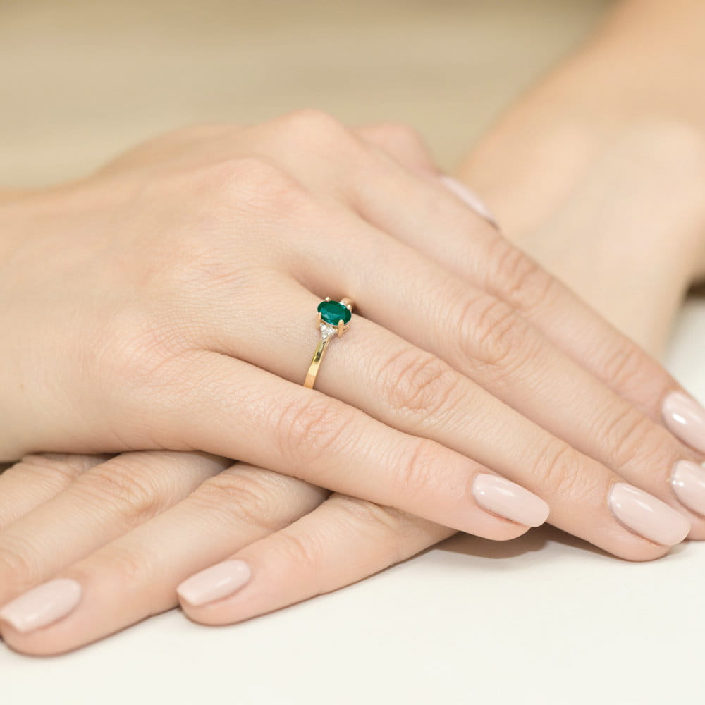 W0301.Z3.EMG.01_4 Złoty pierścionek z zielonym kamieniem na palcu, dłonie z delikatnym manicure w jasnym kolorze.