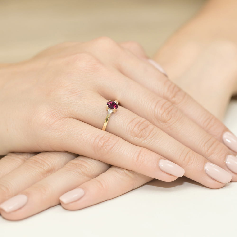 W0301.Z3.RHR.01_4 Na dłoni widoczny złoty pierścionek z rubinem i diamentami, otoczony delikatnymi, zadbanymi paznokciami.