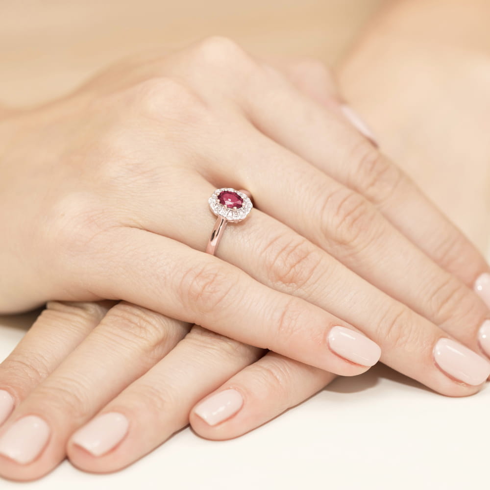 W0304.R3.RUR.01_4 Ręka z pierścionkiem z rubinem otoczonym diamentami, na tle drugiej dłoni z delikatnym manicure.