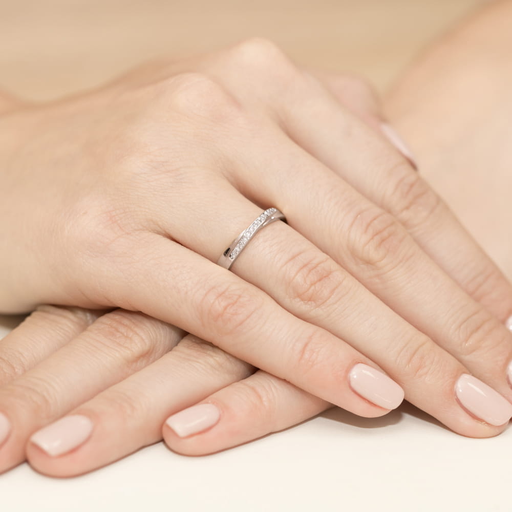 W0305.B3.DIW.01_4 Dwie dłonie z delikatnym pierścionkiem z diamentami, na tle jasnej powierzchni.