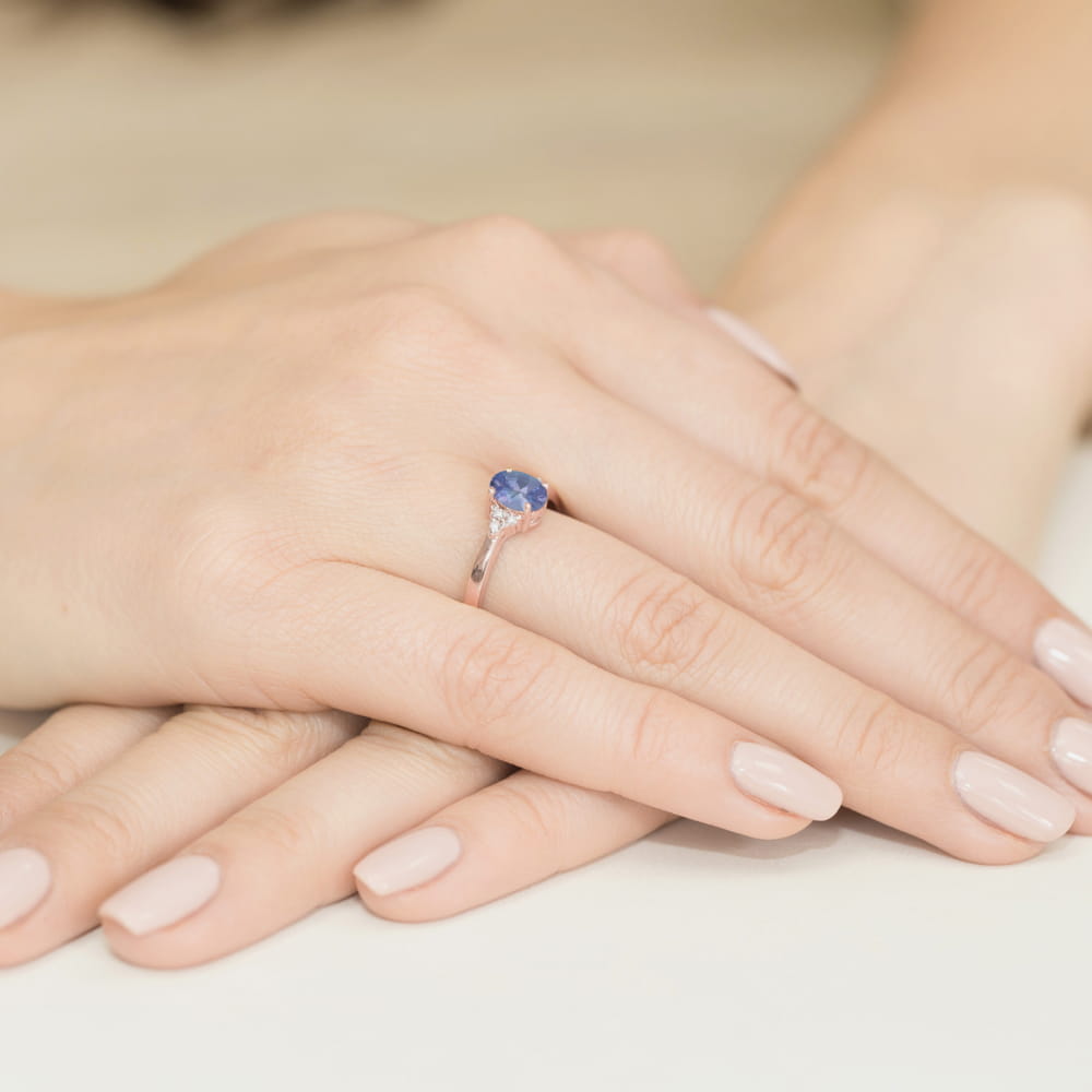 W0308.R3.TAP.01_4 Na dłoni z delikatnym manicure znajduje się pierścionek z niebieskim kamieniem.