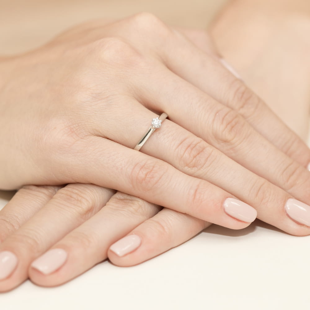 W0311.B3.DIW.01_4 Na dłoni z delikatnym manicure znajduje się srebrny pierścionek z diamentem.