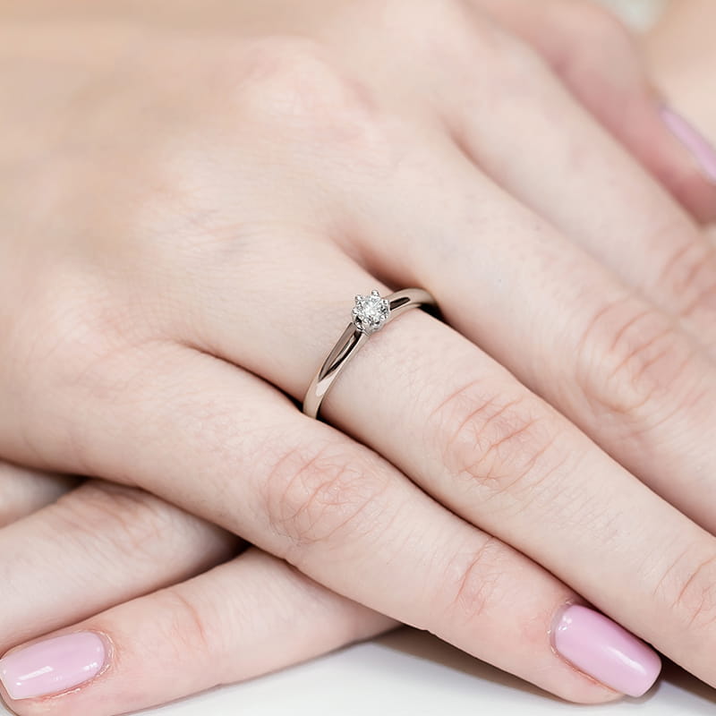 W0317.B3.DIW.01_4 Na dłoni widoczny srebrny pierścionek z diamentem, otoczony delikatnymi, zadbanymi paznokciami.