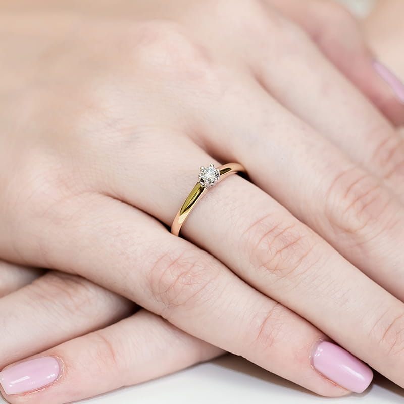 W0317.Z3.DIW.01_4 Złoty pierścionek z diamentem na palcu, dłonie z różowym manicure.