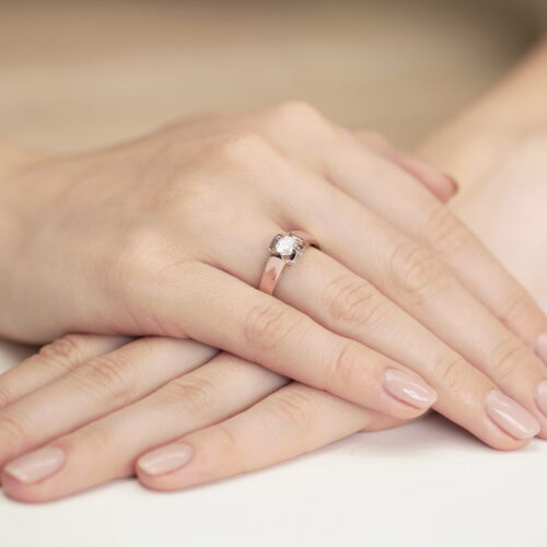 Na dłoniach z delikatnym manicure znajduje się złoty pierścionek z diamentem.