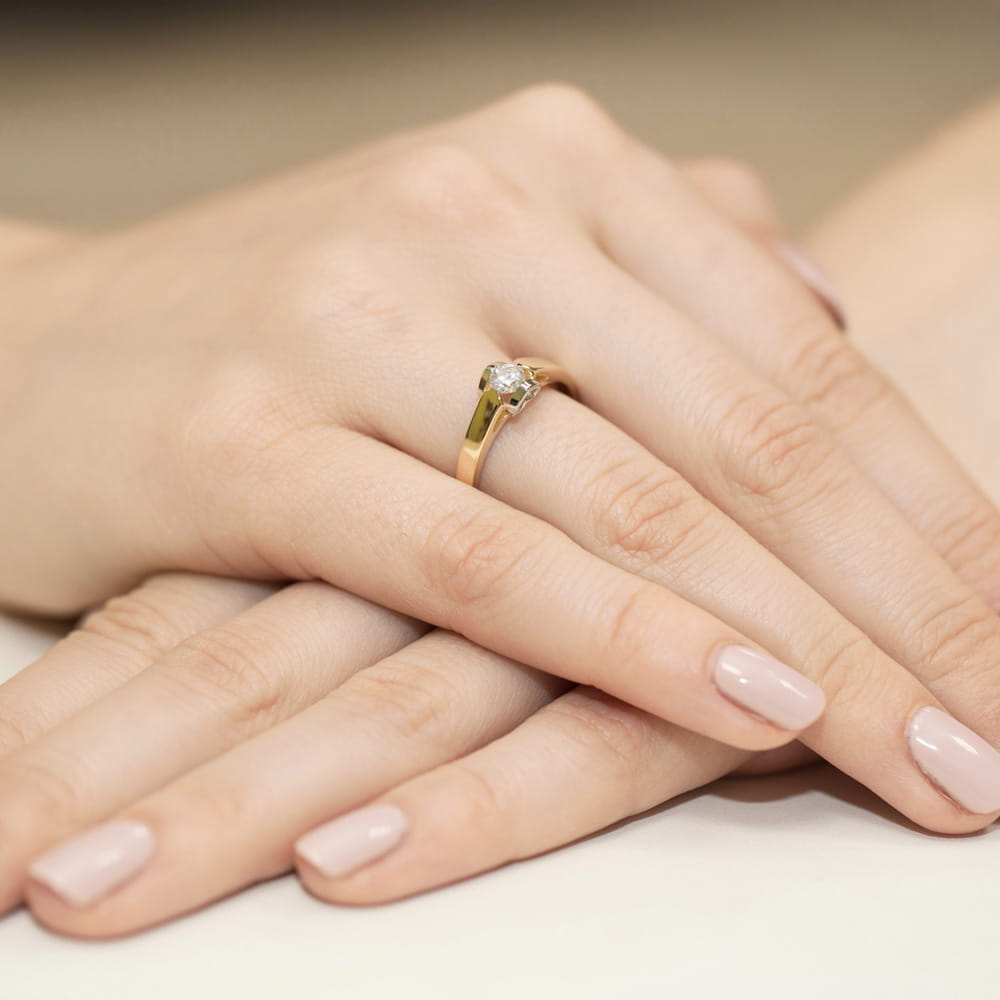 W0320.Z3.LDW.07_4 Złoty pierścionek z diamentem na palcu, dłonie z delikatnym manicure w jasnym kolorze.