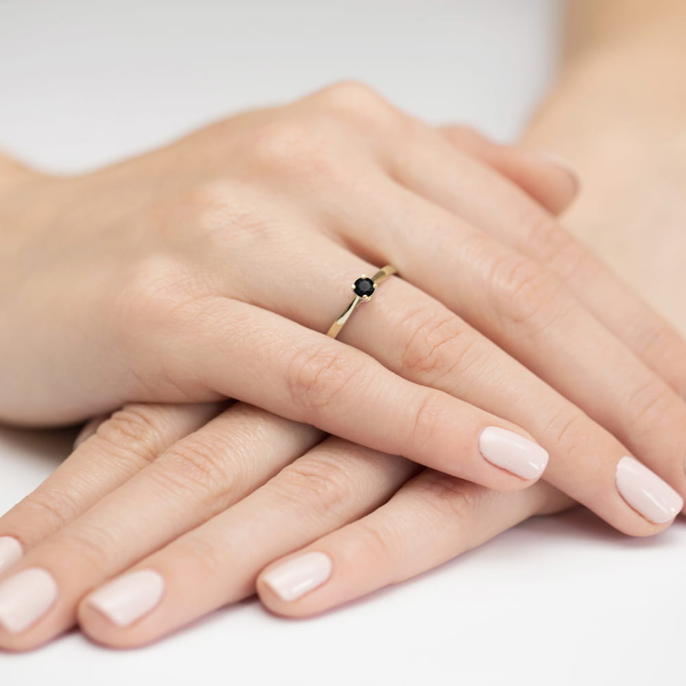 W0335.Z3.DIB.01_4 Złoty pierścionek z czarnym kamieniem na palcu, dłonie z delikatnym manicure w jasnym kolorze.