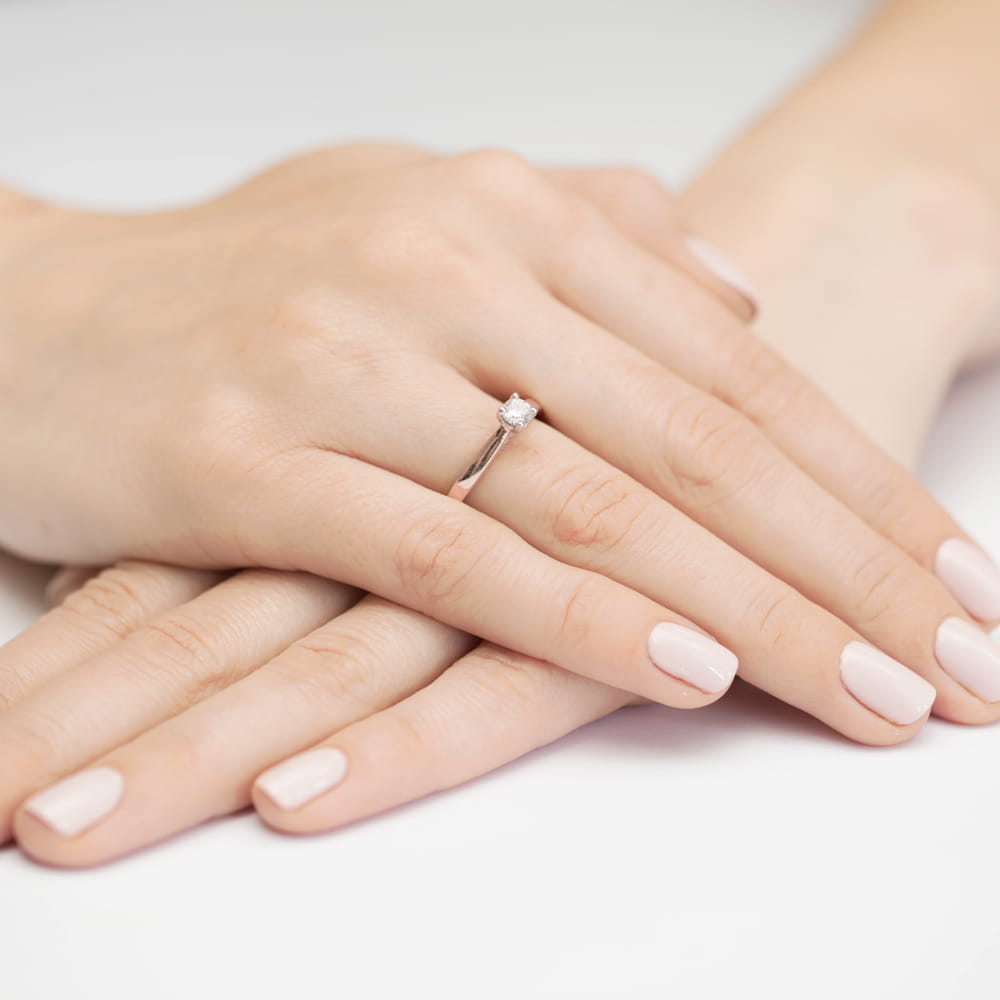 W0341.R3.LDW.01_4 Na dłoni z delikatnym manicure znajduje się srebrny pierścionek z diamentem.