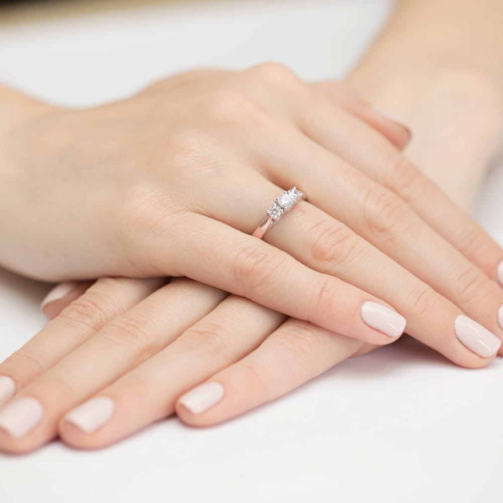 W0344.R3.DIW.01_4 Dwie dłonie z delikatnym manicure, na jednej z nich pierścionek z trzema diamentami.