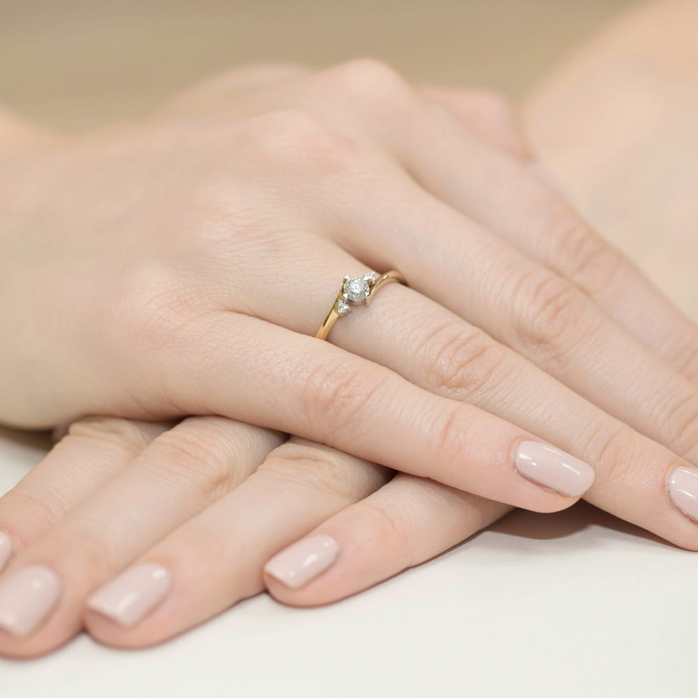 W0346.Z3.DIW.02_4 Złoty pierścionek z diamentem na palcu, dłonie z delikatnym manicure w jasnym kolorze.