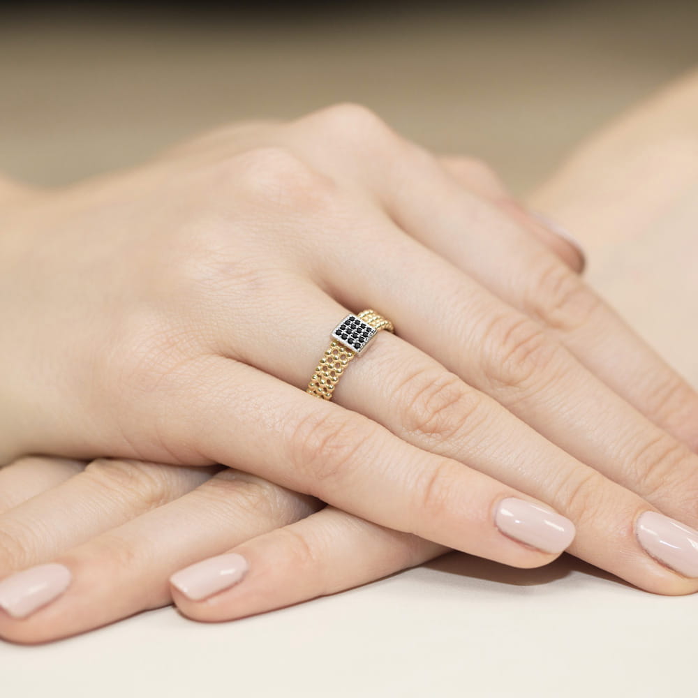 W0353.Z3.DIB.01_4 Złoty pierścionek z czarnymi kamieniami na palcu, dłonie z delikatnym manicure.