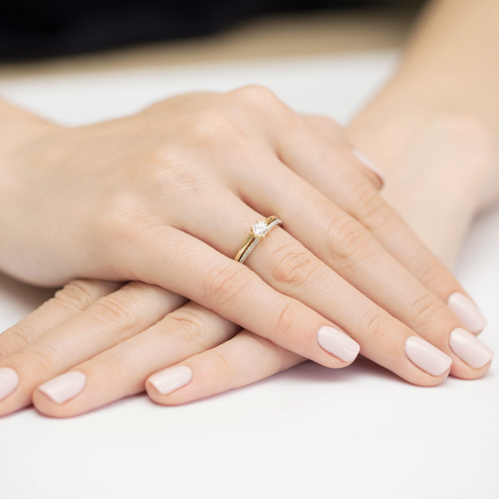 W0355.Z3.DIW.01_4 Złoty pierścionek z diamentem na palcu, dłonie z zadbanymi paznokciami w jasnym kolorze.