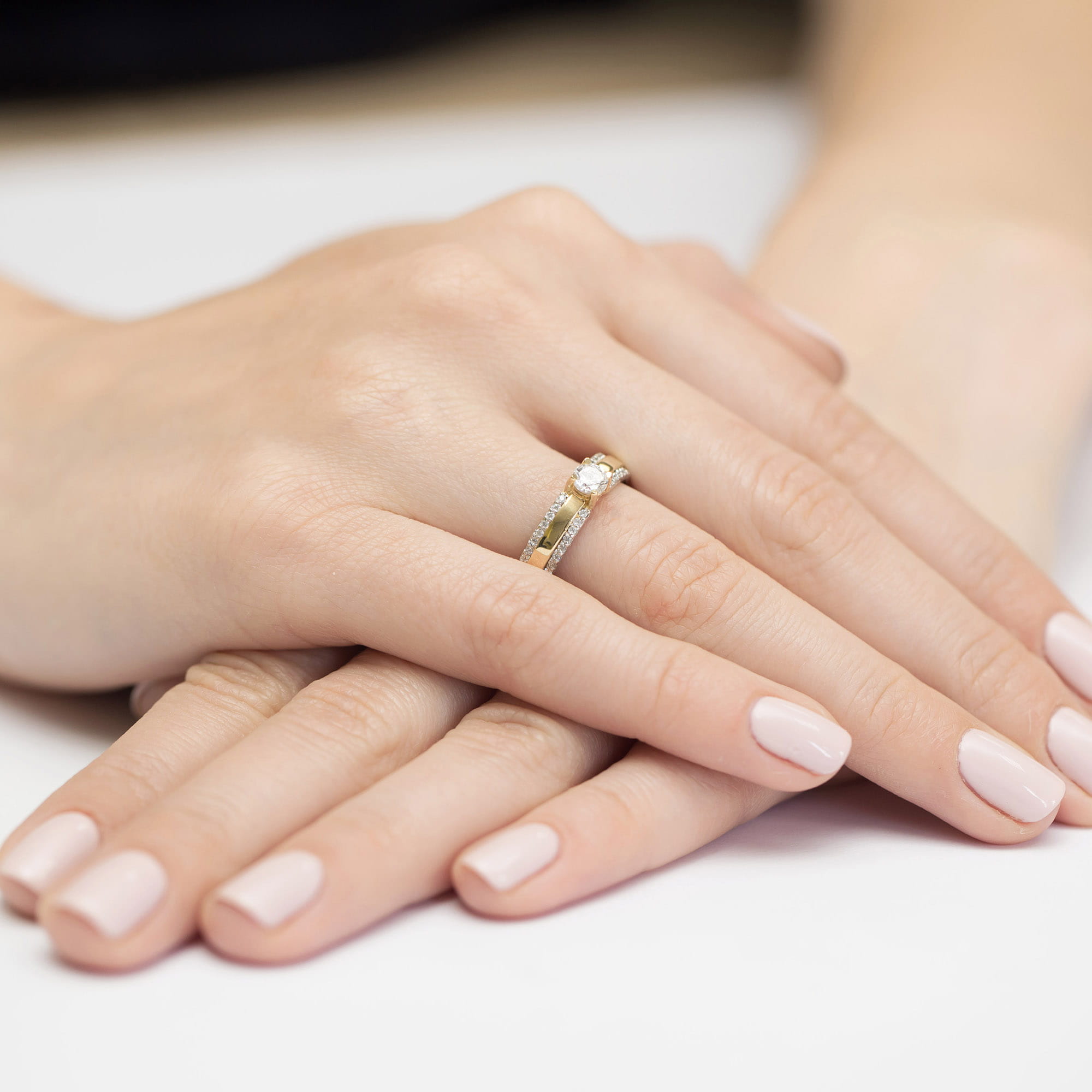 W0356.Z3.LDW.01_4 Na dłoni widać złoty pierścionek z diamentami, otoczony delikatnymi, zadbanymi paznokciami.