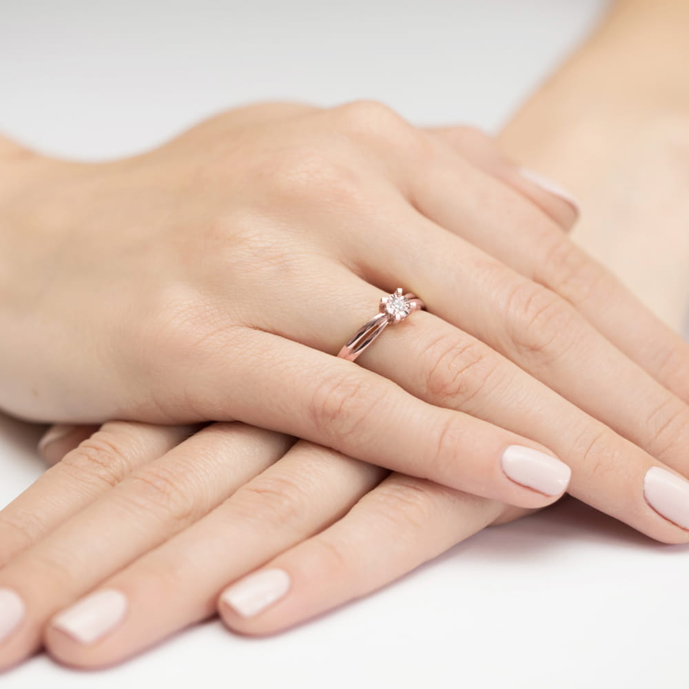 W0360.R3.DIW.01_4 Na dłoni z delikatnym manicure znajduje się pierścionek z diamentem w kształcie kwiatu.