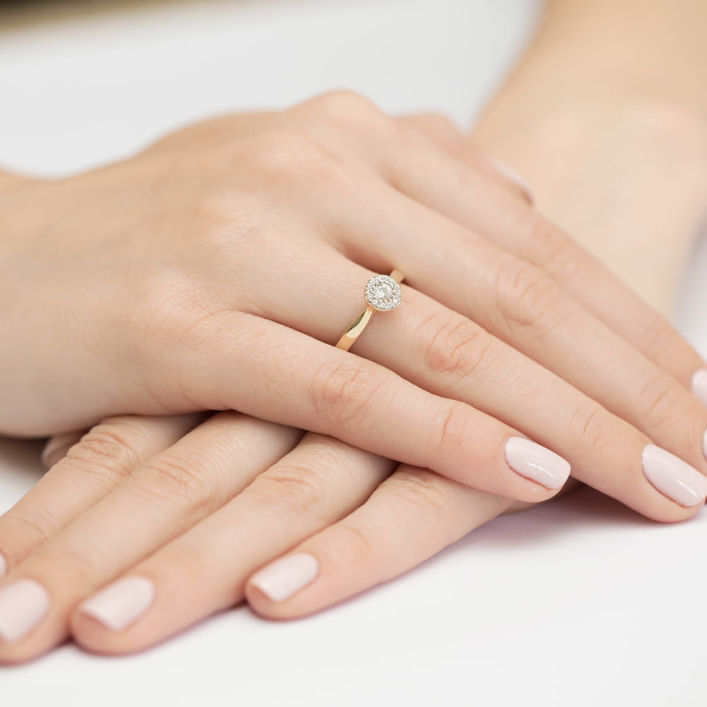 W0362.Z3.LDW.01_4 Na dłoniach z delikatnym manicure znajduje się złoty pierścionek z okrągłym diamentem.