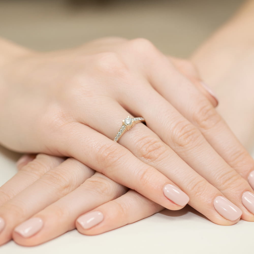 W0364.Z3.DIW.01_4 Na dłoniach z delikatnym manicure znajduje się pierścionek z diamentem.