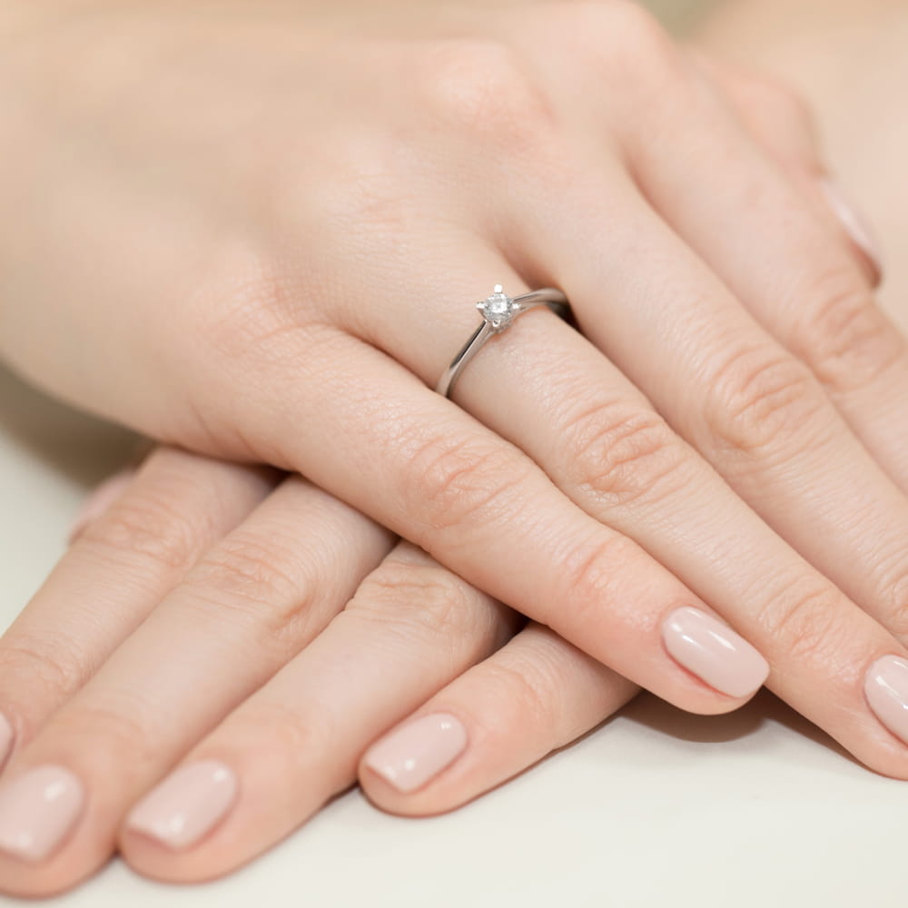 W0367.B3.DIW.01_4 Na dłoniach z delikatnym manicure znajduje się srebrny pierścionek z diamentem.