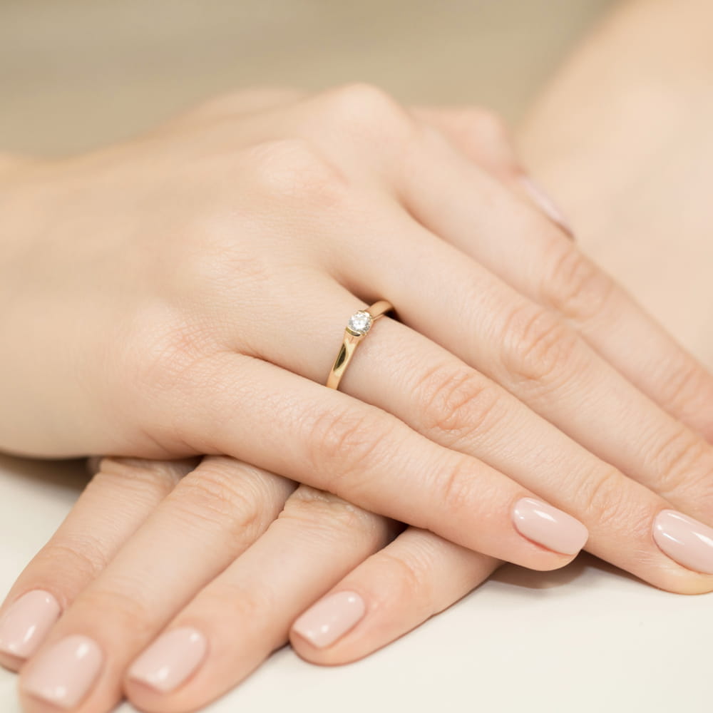 W0369.Z3.LDW.01_4 Złoty pierścionek z diamentem na palcu kobiety, ręce z delikatnym manicure w jasnym kolorze.