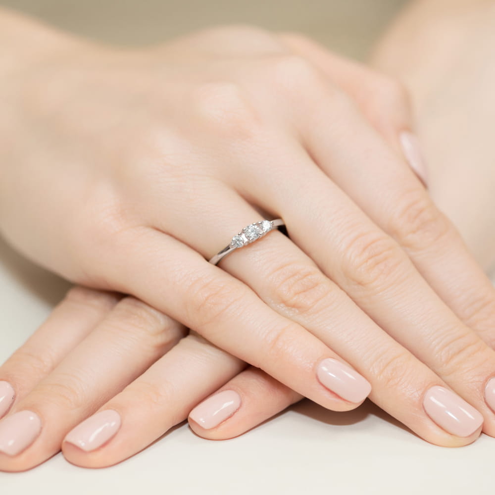 W0377.B3.DIW.01_4 Dwie dłonie z delikatnym pierścionkiem na jednym z palców, paznokcie w jasnym kolorze.