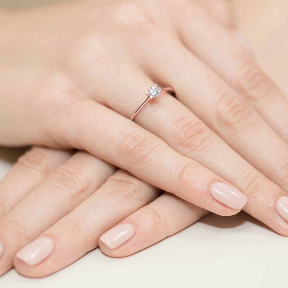 W0387.R3.DIW.01_4 Na dłoni z delikatnym manicure znajduje się pierścionek z diamentem.