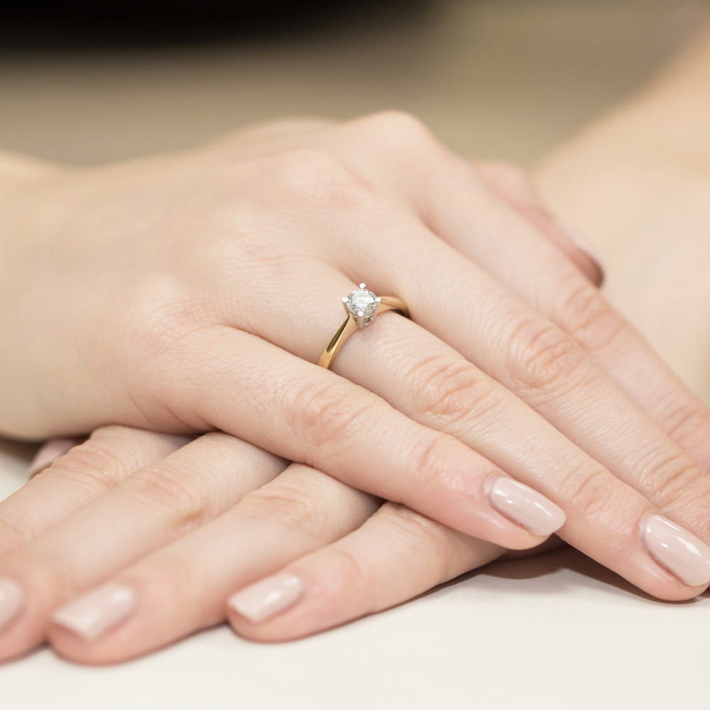 W0404.Z3.LDW.01_4 Złoty pierścionek z diamentem na palcu, dłonie z delikatnym manicure w neutralnym kolorze.