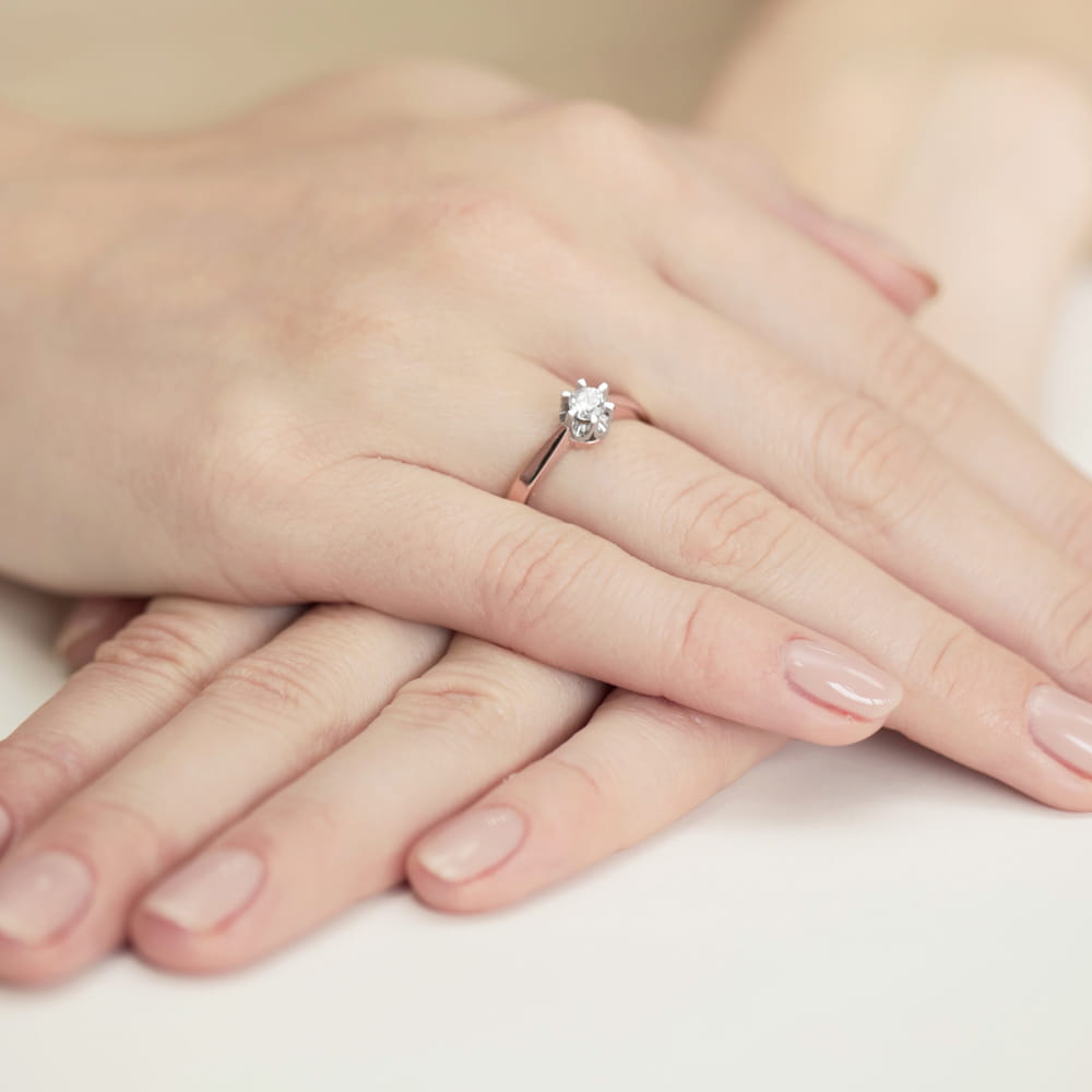 W0408.R3.DIW.02_4 Dwie dłonie z delikatnym manicure, jedna z pierścionkiem zaręczynowym z dużym diamentem.