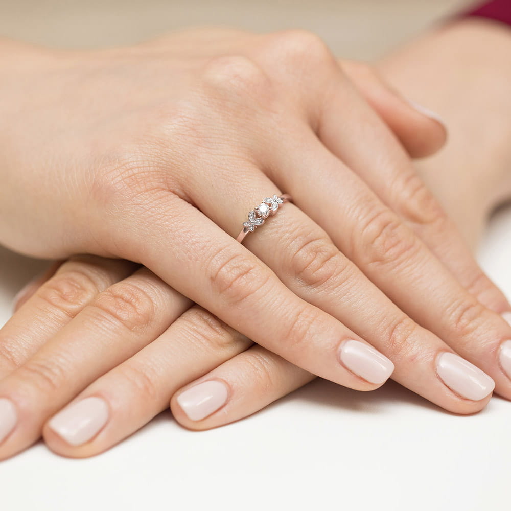 W0414.R3.DIW.01_4 Na dłoni z delikatnym manicure znajduje się srebrny pierścionek z trzema błyszczącymi kamieniami.