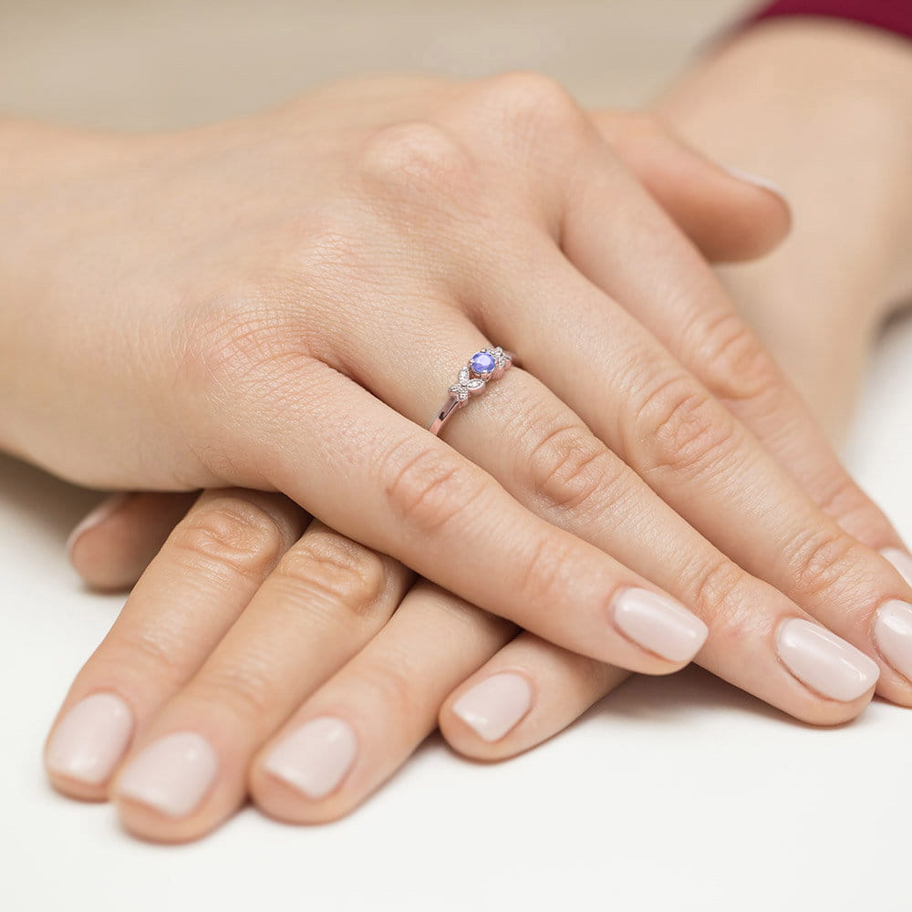 W0414.R3.TAP.01_4 Dwie dłonie z delikatnym pierścionkiem na palcu, z niebieskim kamieniem i jasnym manicure.