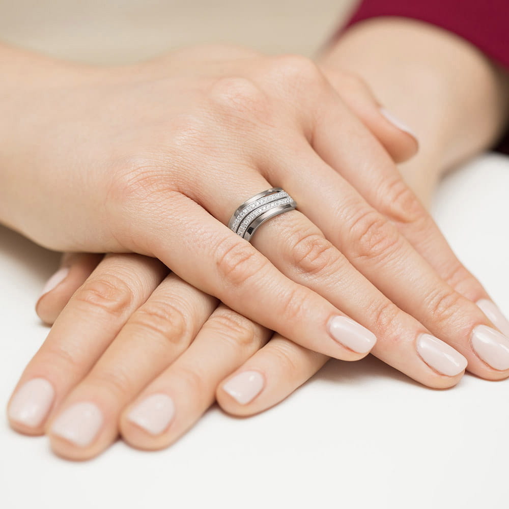 W0416.B3.DIW.01_4 Dwie dłonie z delikatnym manicure, trzymające pierścionek z diamentami na palcu.